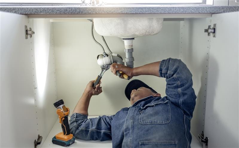Plumber repairing pipes beneath a bathroom sink in Peachtree Corners